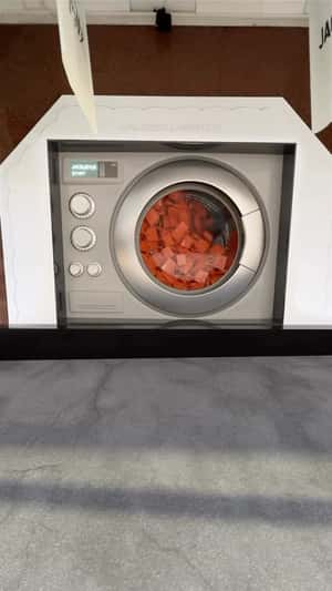 Orange Bags Spill Out of Washer Dryer in fake-out-of-home ad of Jacquemus