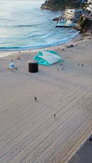 Giant Inflated Perfume Bottle on Beach Shoreline in a fake-out-of-home ad of Who is Elijah