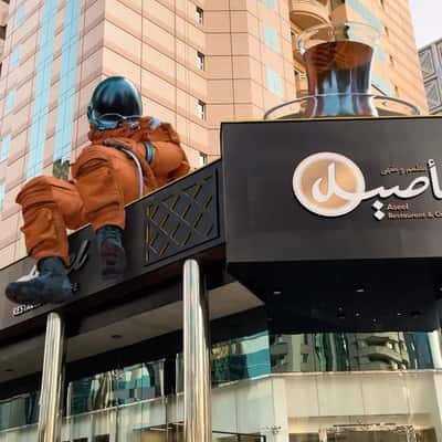 Astronaut Sitting on Cafe in a fake-out-of-home ad of Aseel Restaurant